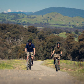 Two cyclists riding the gravel route of Goin to Bonnie Doon past hills and farmland.